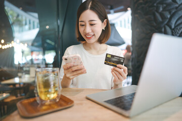 Young adult asian woman using credit card with internet banking mobile app sitting at cafe