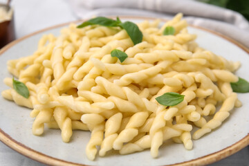 Plate of delicious trofie pasta with basil leaves on table, closeup