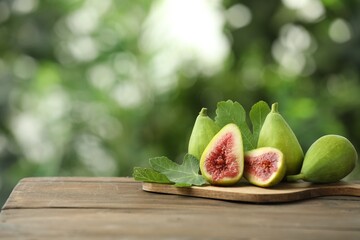 Cut and whole green figs on wooden table against blurred background, space for text
