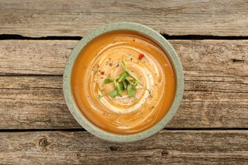 Delicious pumpkin soup with microgreens in bowl on wooden table, top view