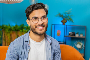 Portrait of happy calm Indian man at home couch smiling friendly, glad expression looking away dreaming resting, relaxation feel satisfied good news, celebrate win. Arabian Hindu guy in living room