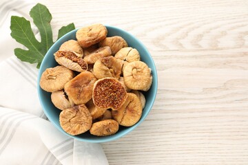 Bowl with tasty dried figs and green leaf on white wooden table, flat lay. Space for text
