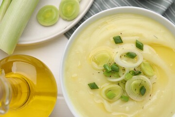 Bowl of tasty cream soup with leek on wooden table, flat lay