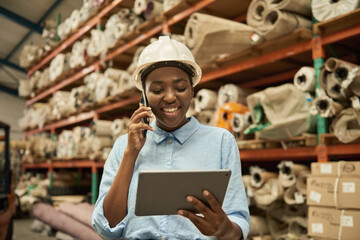 Smiling African woman using a tablet and cellphone in a warehouse - obrazy, fototapety, plakaty
