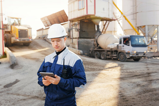 Engineer man in uniform use tablet computer for controls loading of cement to mixer truck on concrete factory. Concept automated industry logistics with online