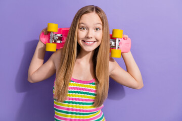 Photo of cool positive schoolgirl with straight hairdo dressed striped top hold skateboard behind head isolated on violet background