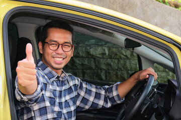Adult Asian man smiling and give thumb up from inside a car