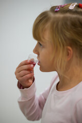 little girl in pajamas takes red cough medicine, blurred background