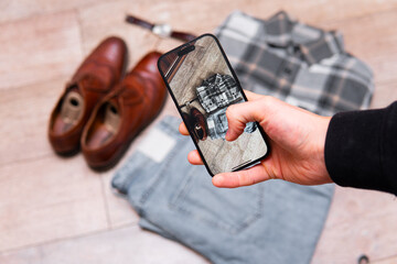 a man takes a photo of clothes using a smartphone. Selling second-hand clothes online