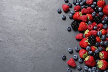 Many different fresh ripe berries on dark grey table, flat lay. Space for text
