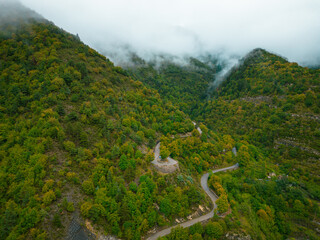 View from drone to Col de Turini, french alps pass. Foggy rainy day on a mountains. Curvy tarmac road.