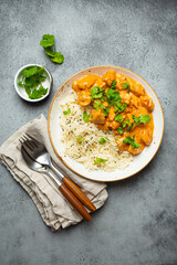Traditional Indian dish chicken curry with basmati rice and fresh cilantro on rustic white plate on gray concrete table background from above. Indian dinner meal