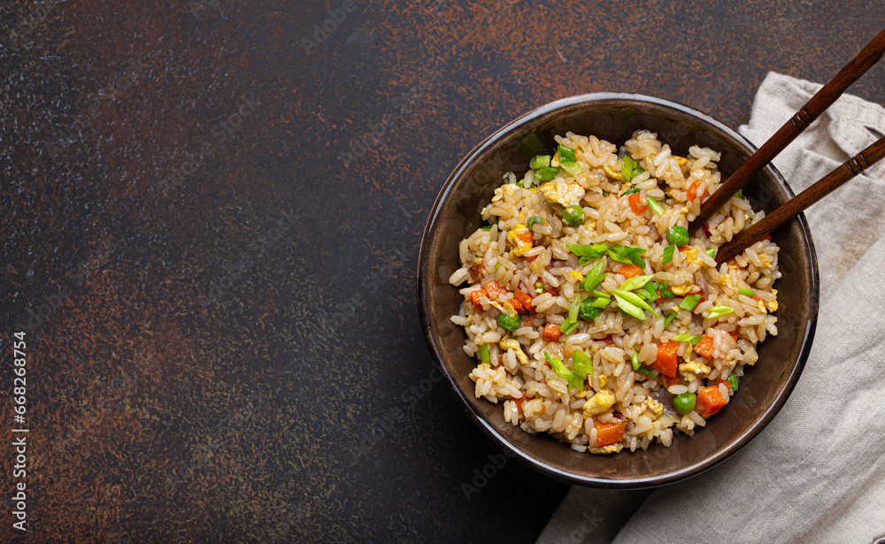 Poster authentic chinese and asian fried rice with egg and vegetables in ceramic brown bowl top view on dar