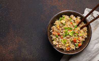 Authentic Chinese and Asian fried rice with egg and vegetables in ceramic brown bowl top view on dark rustic concrete table background. Traditional dish of China, space for text