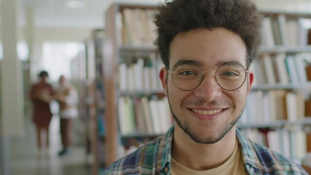 Medium closeup portrait of young Biracial male migrant student smiling at camera on blurred library background