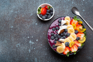 Healthy summer acai smoothie bowl with chia seeds, fresh banana, strawberry, blueberry, cocos, kiwi top view on rustic concrete background with spoon. Space for text