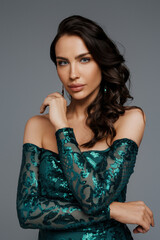 Stunning brunette with a voluminous hairstyle in a graceful green evening gown against a gray backdrop