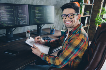 Portrait of smart positive front end developer guy sitting chair hold pen write clipboard pc...