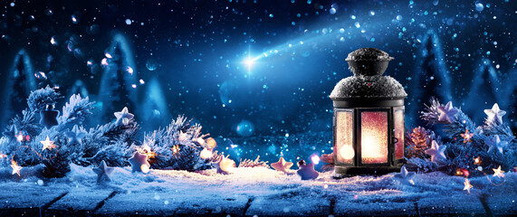 A lamp shining with warm light against the background of a winter forest and the night sky with a...