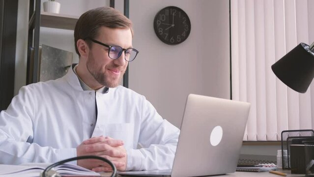 Upbeat male doctor consulting patient online via webcam video call on laptop computer.