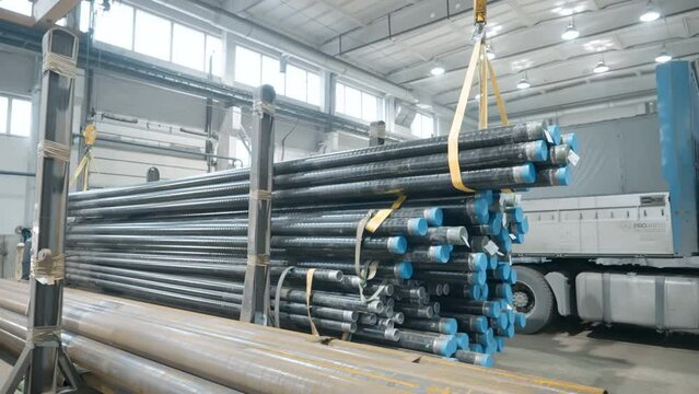 Huge amount of steel pipes loaded on the industrial factory crane machine. Lots of metal pipes manufactured at the industrial factory. Lifting up stacks of pipes made at industrial factory