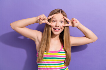 Fototapeta premium Photo of optimistic positive schoolgirl with straight hairdo dressed striped top showing v-sign on eyes isolated on violet background