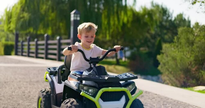 A child driving a toy electric car in a park on a summer day