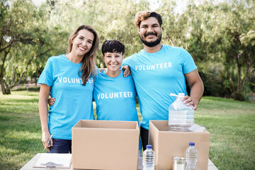 Multiracial team of volunteers working collecting goods and food for community service outdoors -...