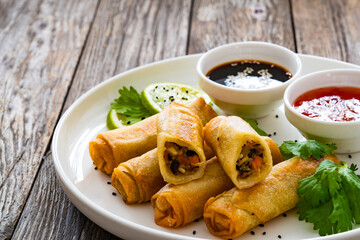 Vegetable filled spring rolls and sauces on wooden table
