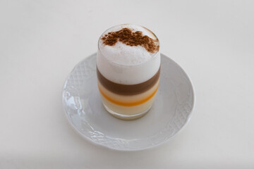 Delicious glass of a Barraquito coffee, with liquor, milk and cinnamon. Typical of Tenerife, Canary Islands.. Aesthetic coffee with layers. Santa Cruz de Tenerife. Background a white table