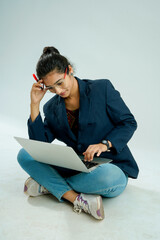 indian girl seated on a white background balances a laptop on her lap