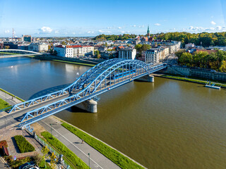 Krakow, Poland. Pilsudski blue tied arc bridge over Vistula River with tramway,  blue tram, sidewalk and bicycle lane. Boulevards on riverbanks. Podgorze district in the background. Aerial view