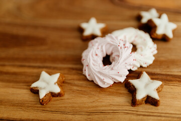 New Year background for winter cards. Gingerbread cookies in the shape of stars and pink meringue cookies lie on a brown background with Christmas lights. Delicious sweet pastries on a wood table