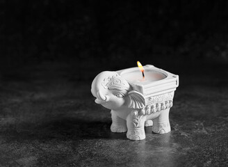 Elephant-shaped candlestick with a burning candle on a black background, front view, low key, selective focus.