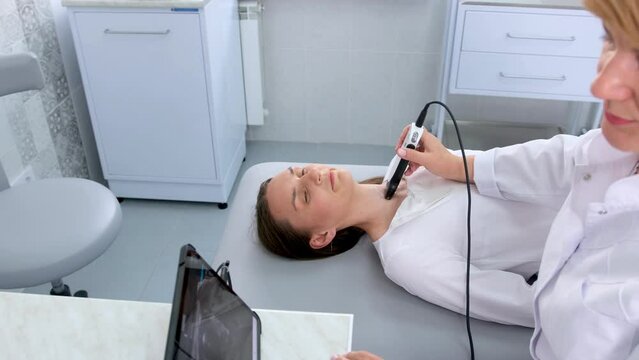a doctor in a modern diagnostic clinic examines the thyroid gland of a patient of a young attractive woman on an ultrasound machine. Prevention of thyroid cancer