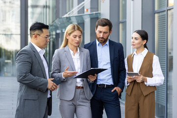 Four business people discussing financial results of achievement, mature men and women outside office building discussing success strategy, diverse team of businessmen and businesswomen in suits