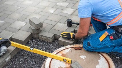Laying interlocking paving. A worker's hand is placing interlocking paving stones around the sewer manhole cover.