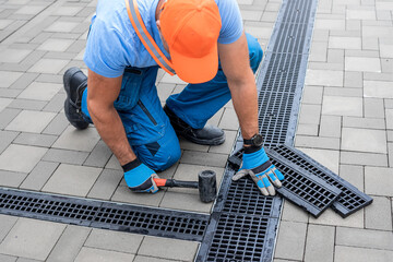 Laying interlocking paving. A worker's hand is placing drainage channel on an area made of...