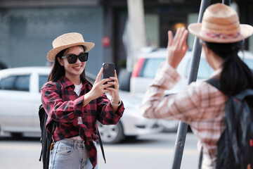 Asian female tourist takes a photo of a female friend while touring the city center. - obrazy, fototapety, plakaty