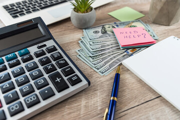 stiket with text need help, dolar and laptop on office desk.