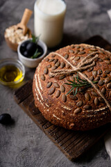 Baked sourdough bread from whole grain flour and pumpkin seeds on a grid, olive oil and black olive on a rustic wooden table. Artisan bread.