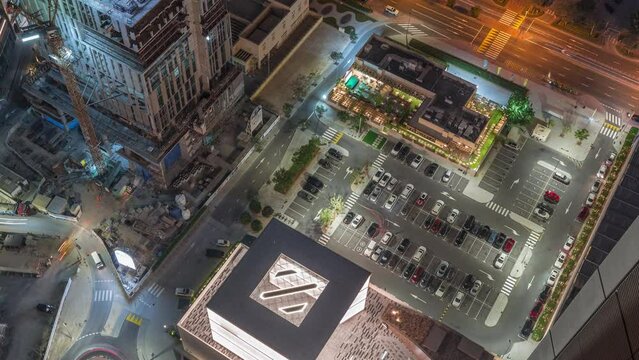 Construction site with cranes and parking lot near shopping avenue in Dubai aerial night timelapse, UAE. Towers in financial district from above. Traffic on a road