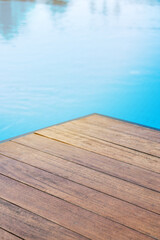 Fototapeta premium Empty wooden tabletop in front of a swimming pool with blue tiles. Concept for product presentation display with summer background.