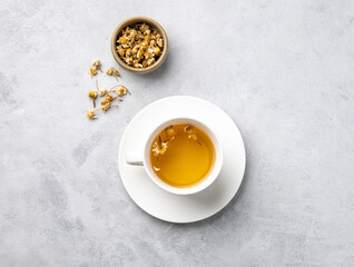 Chamomile herbal tea in a white cup on a light background with dry flowers. The concept of a...