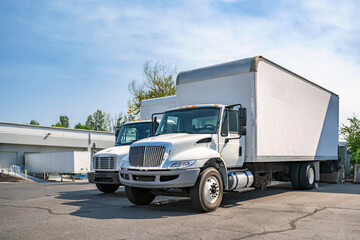Middle duty compact rig semi trucks with box trailers standing on the warehouse parking lot take a...