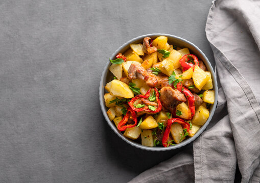 Fried pork meat with potatoes, onions and peppers. National homemade Georgian dish ojakhuri in a bowl on a dark background with napkin.