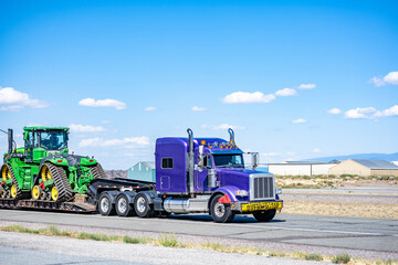 Oversize cargo hauler big rig purple classic semi truck tractor transporting oversize load on step...