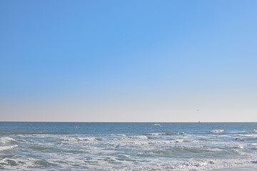 Background, clear blue sky, sea, waves crashing on the shore, seagulls flying low over the sea