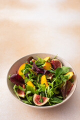 Salad with mixed lettuce and peaches with figs, plate with salad on beige background