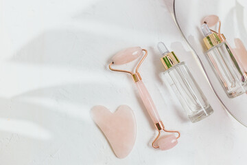 Facial roller from crystal rose quartz and massage tool jade on beige background with dry flowers....
